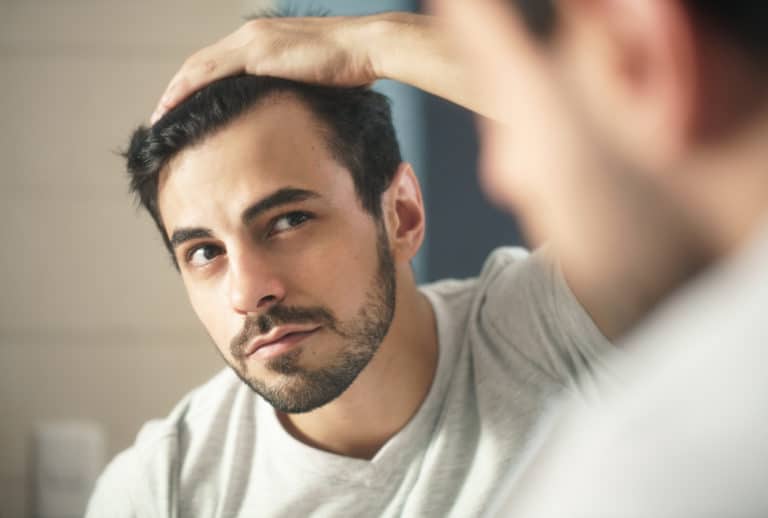 The man is carefully combing his hair in front of a mirror.
