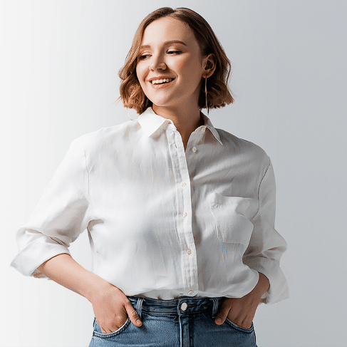 A person with short, light brown hair wearing a white button-up shirt and blue jeans looks to the side with hands in pockets, smiling, perhaps pondering the benefits of compounded medications.